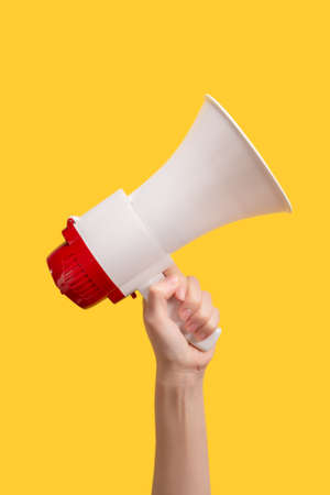 Megaphone in woman hands on a yellow background. Copy space.の写真素材