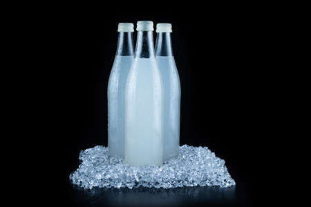 A white bottle with a soda drink on ice on a black background.