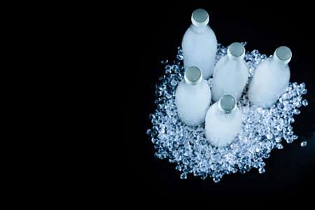 A white bottle with a soda drink on ice on a black background.の写真素材