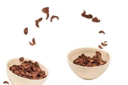 Chocolate corn flakes falling to the white bowl isolated on white. Motion. Copyspace.