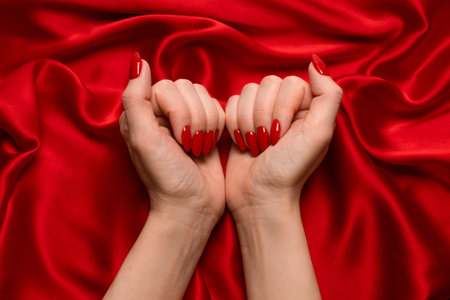 Beautiful red manicure on woman hands on a luxury red silk backround.の写真素材
