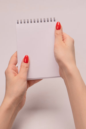 A notebook with empty white paper in woman hands with red nails. copyspace.の写真素材