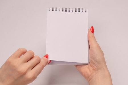 A notebook with empty white paper in woman hands with red nails. copyspace.