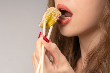Young woman with red nails is eating sushi close up.