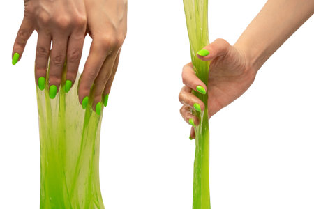 Green slime toy in woman hand with green nails isolated on a white background.の写真素材