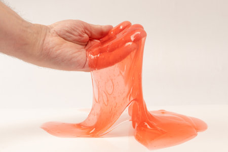 Red slime toy in man hand isolated on white. Top view.