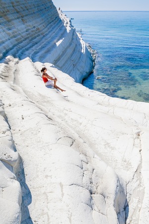A girl sits on a slope of white cliff called "Scala dei Turchi" in Sicily, near Agrigento. Italyの写真素材
