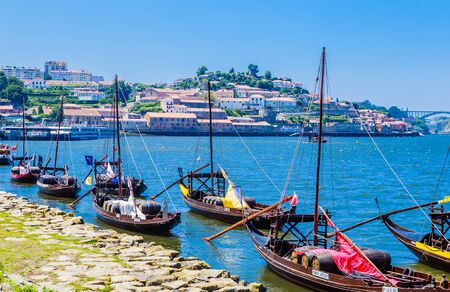 Typical portuguese wooden boats, called "barcos rabelos" transporting wine barrels on the river Douro with view on Villa Nova de Gaia in Porto, Portugalの写真素材