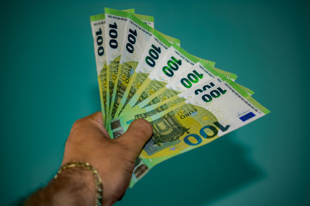Hand Holding Fan of 100 Euro Banknotes on Green Background - Wealth, Finance, Cash Money, European...