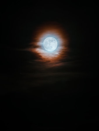 Mystical full moon glowing in the night sky, surrounded by thin clouds and a colorful halo. A...