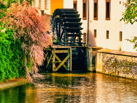 Historic Watermill with a Large Water Wheel on a Calm River, Surrounded by Lush Vegetation and...