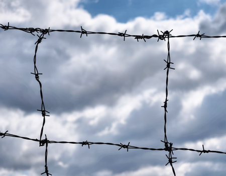 Striking Barbed Wire Fence Against a Cloudy Sky â A Powerful Symbol of Boundaries and Isolation in Nature and Security Imageryの写真素材