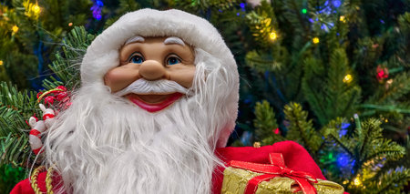 Santa Claus doll with a gift box on the background of the Christmas treeの写真素材