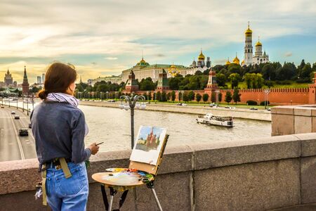 MOSCOW, RUSSIA - 20.09.2017. A young artist paints a landscape on a bridge near the Moscow Kremlin on a warm autumn day, and a motor ship floats along the riverのeditorial素材
