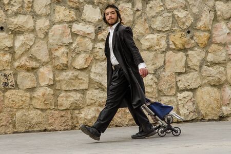 JERUSALEM, ISRAEL, 05.04.2018: Walk of an Orthodox Jewish boy with pace in a black frock coat, with...