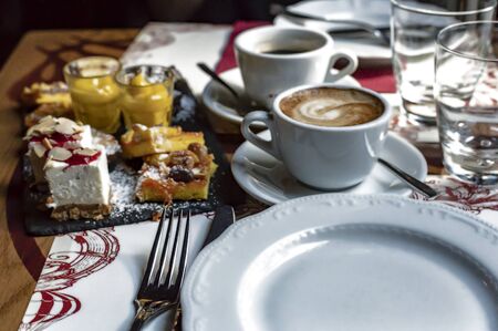Dessert mix chocolate brownie cheese cream cake with peanuts and almonds sprinkled with powdered sugar two cups of coffee Americano and cappuccinoの写真素材