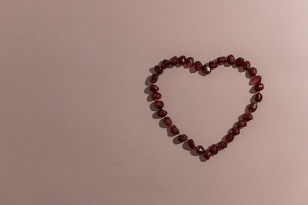 Heart made from pomegranate seeds, unfilled, with a light shadow on a pink background. Horizontal top view.の写真素材