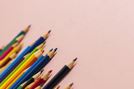 Multi-colored pencils of different lengths on a pink background, located on the left corner, extending into the distance. Horizontal close-up.の写真素材