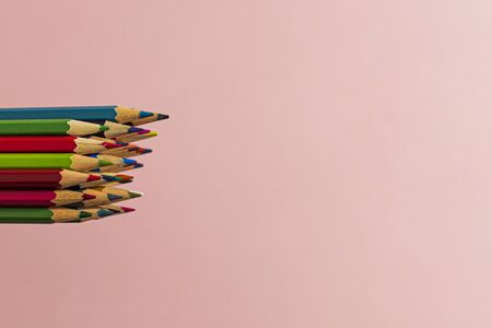 Multi-colored pencils located together in the left side on a pink background. Horizontal close-up.