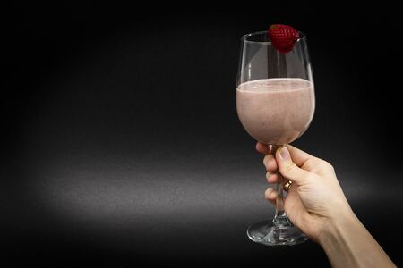 The girl holds in her hand a natural cocktail in a wine glass, with one strawberry on top. Black background. Horizontal view. Close-up. Copy spaceの写真素材