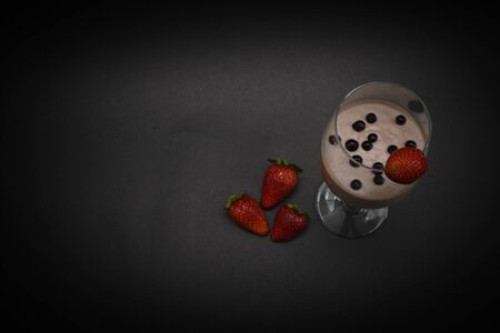 Fruit smoothie in a wine glass with natural blueberries in a drink with one strawberry on top and three strawberries on the bottom. Black background. Horizontal view. Close-up. Copy space. Top view.の写真素材