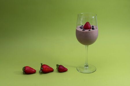 Organic vitamin fresh smoothie in a glass with natural blueberries and one strawberry in the drink and with three strawberries in a row from the bottom, as if in the direction. Green light background.の写真素材