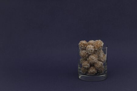 Natural energy balls in coconut flakes in a glass transparent glass on a dark purple background....