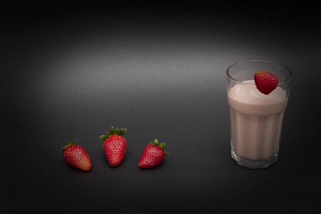 A healthy smoothie in a glass with one strawberry on top and three strawberries on the bottom. Dark background. Horizontal view. Close-up. Copy spaceの写真素材