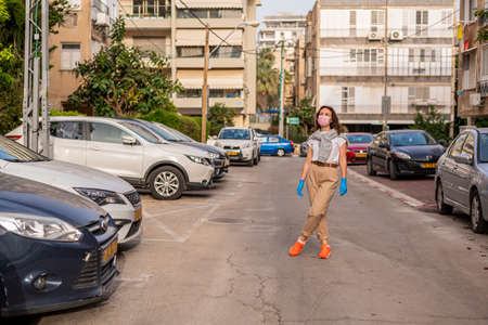 A beautiful and young girl walks along a city street during a pandemic or epidemic. She stands and...
