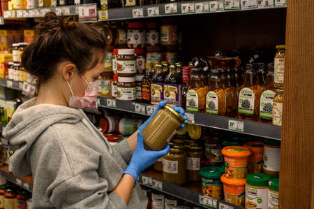In a large supermarket. The girl chooses her products, as she will be in quarantine. She is wearing a protective mask and gloves. A limited number of people inside the grocery store. Minimal protection in the form of masks and gloves. Self-monitoring and のeditorial素材