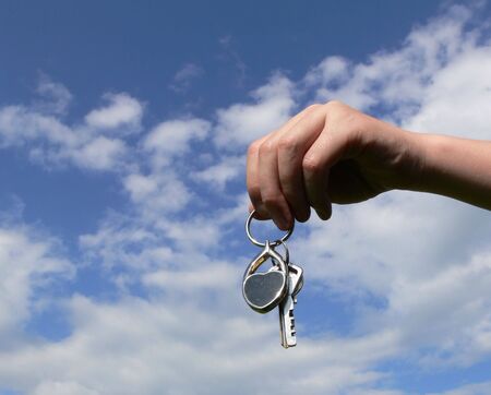 Hand and keys on blue sky with cloudsの写真素材