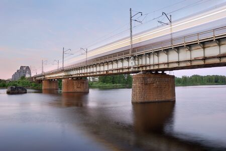 The moving express train on the bridge across Daugava river.の写真素材