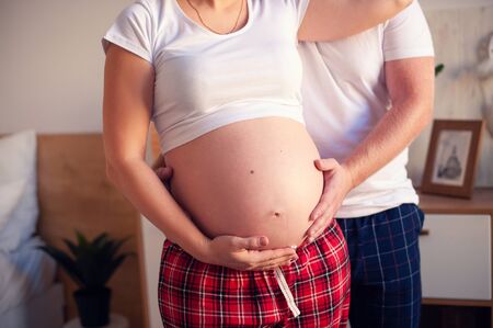 Cropped image of beautiful pregnant woman and her handsome husband hugging the tummy