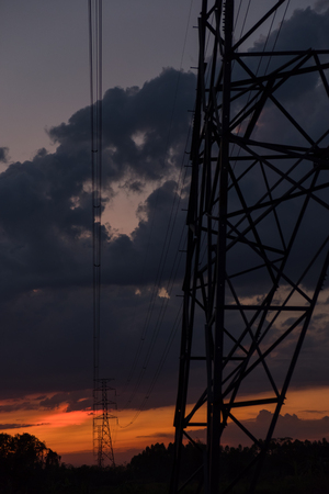 High voltage electricity transmission pylon silhouette with power plant against dark lights sky.の写真素材