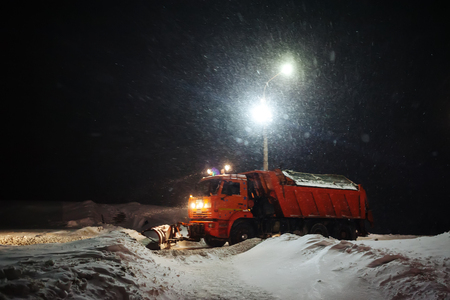 snow plow machine clears snow outside at night during snowstormの写真素材