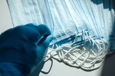 A hand in a blue latex glove takes a white medical mask