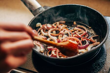 Onions are fried in a pan. Female hand stirs the onion.の写真素材