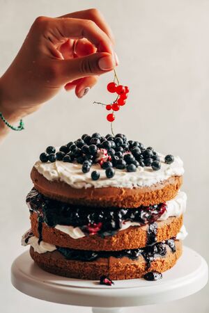 A female hand decorates a cake with fresh berries.