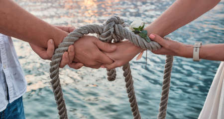 close-up. Hands tied with sea rope against backdrop of sea water at sunset. An oath with hands as a...