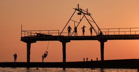 Silhouette, shadow drawing of people resting on an amazing sunset of day silhouette, swing on rope, jump into the water .Active leisure at sea.の写真素材