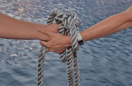 close-up. Hands tied with sea rope against backdrop of sea water at sunset. An oath with hands as a sign of eternal love and reverence. Valentine's day concept, wedding ceremony, farewell, anniversaryの写真素材