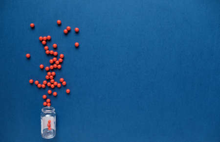 Red round, balls, pills spill out of an inverted transparent bottle with pills on blue background.の写真素材