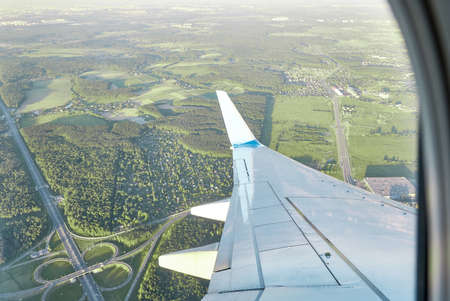 View of wing of an airplane flying at high altitude against background of green terrain.の写真素材