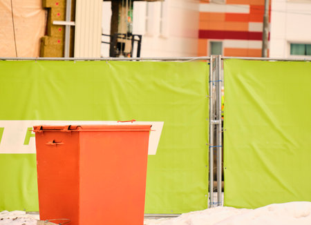 Colorful orange dumpster with waste behind green fence. Garbage sorting. Responsible attitude towards environment.の写真素材