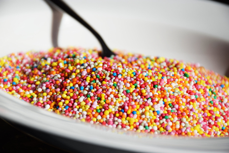 Colourful sweet hungdreds and thousands candy in a white bowl with a spoon, ideal for addiction...