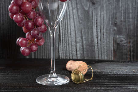 Bunch of red grapes and champagne glass with dark wood background