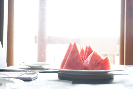 Close-up of fresh slices of red watermelon on plate on table with sunlight backgroundの写真素材