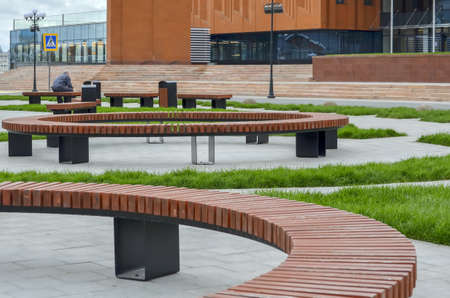 Kazan, Russia, September 16, 2020. Round wooden benches in front of the entrance to a modern buildingのeditorial素材