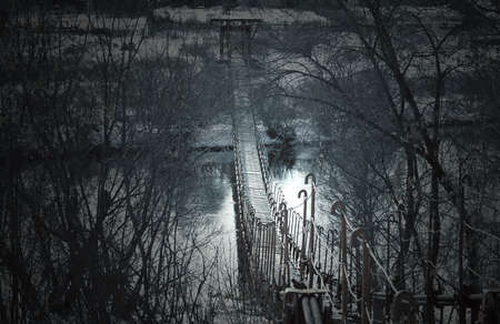 Creepy dark old suspension bridge across the river in the fog. Background for halloween.の写真素材