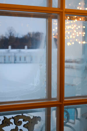 A view of the winter courtyard through the frosty window, the reflection of the shining chandelier...